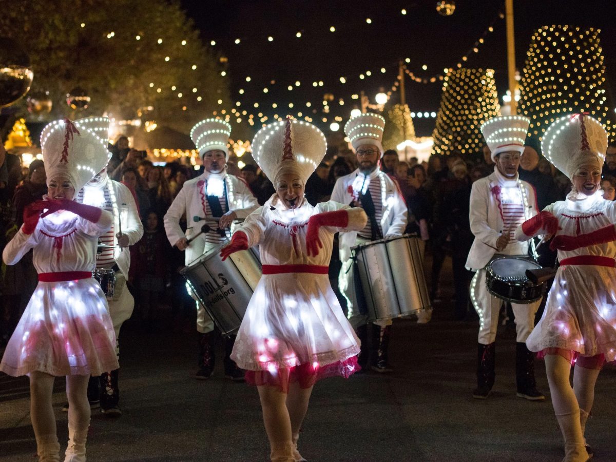 Umzug leuchtender Künstler und Blaskapelle im Herzen des Weihnachtsmarktes Noël au Quai in Genf