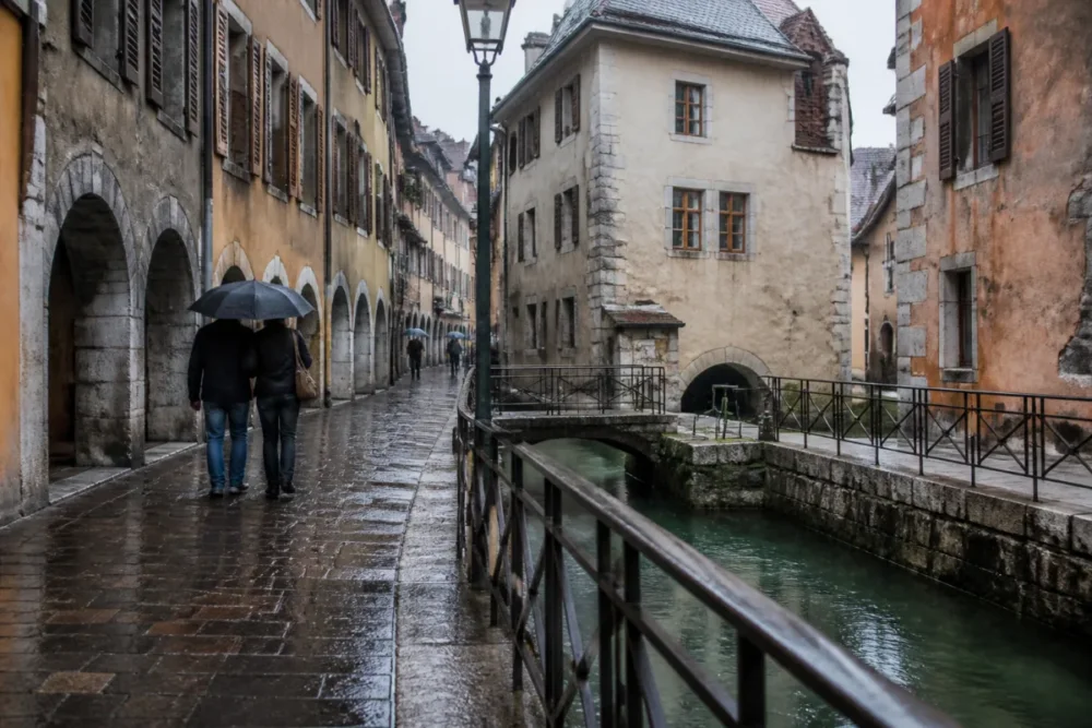 Photo réaliste de la vieille ville d’Annecy sous la pluie avec arcades et canaux