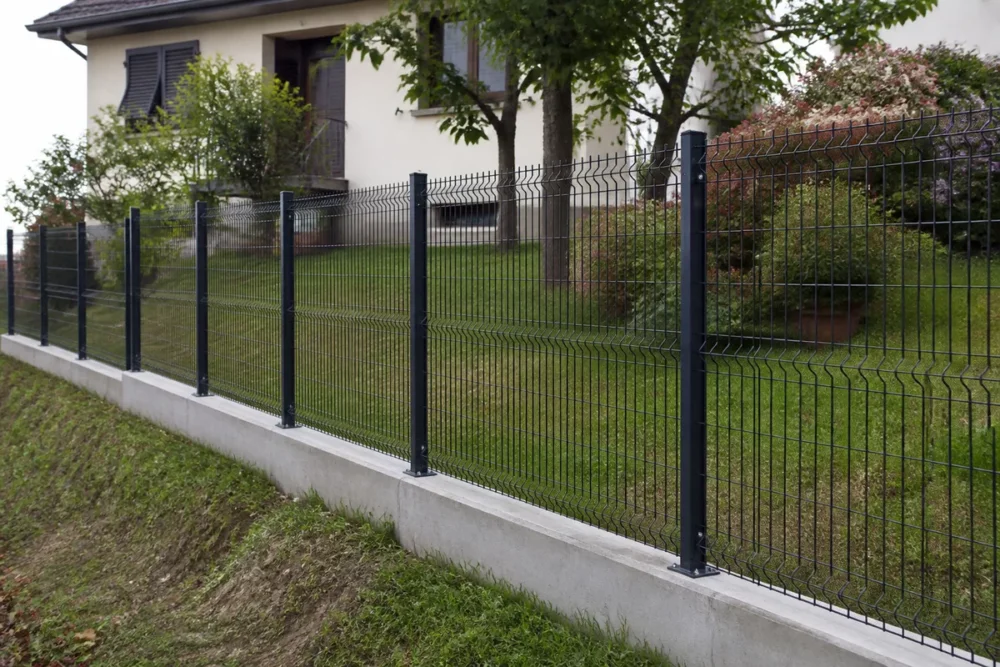Photo réaliste d’une clôture rigide avec soubassement béton installée sur un terrain en pente.