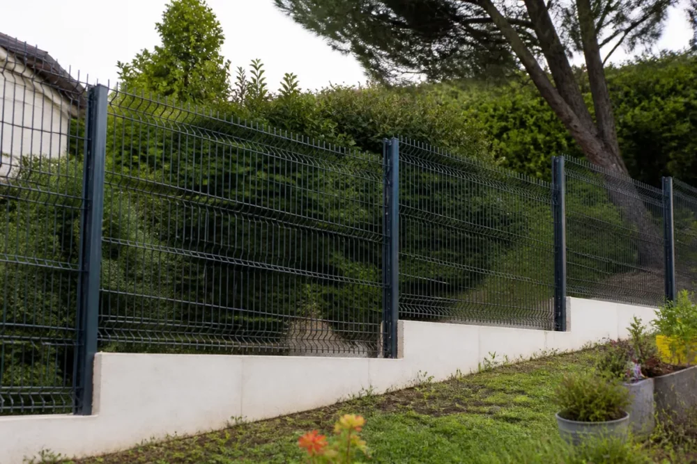 Clôture rigide posée sur un terrain de jardin en pente avec poteaux et soubassement