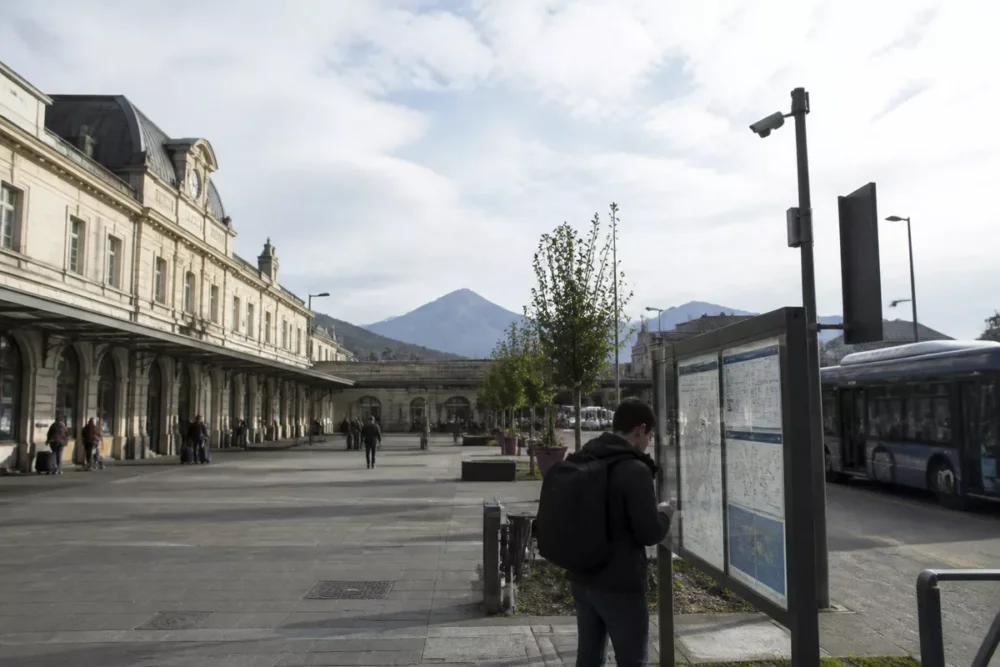 Gare de Tarbes à l’arrivée d’un train avec un voyageur consultant un horaire de bus vers Bagnères-de-Bigorre