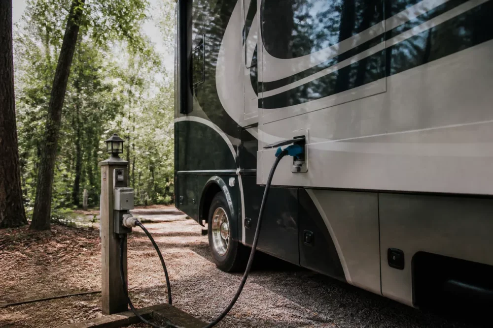 Photo réaliste d’un camping-car branché à une borne électrique sur un emplacement de camping