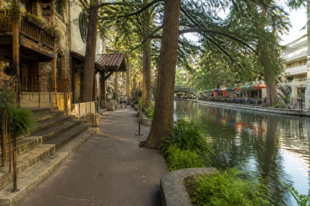 Vue réaliste du River Walk de San Antonio avec ses quais, façades historiques et arbres.