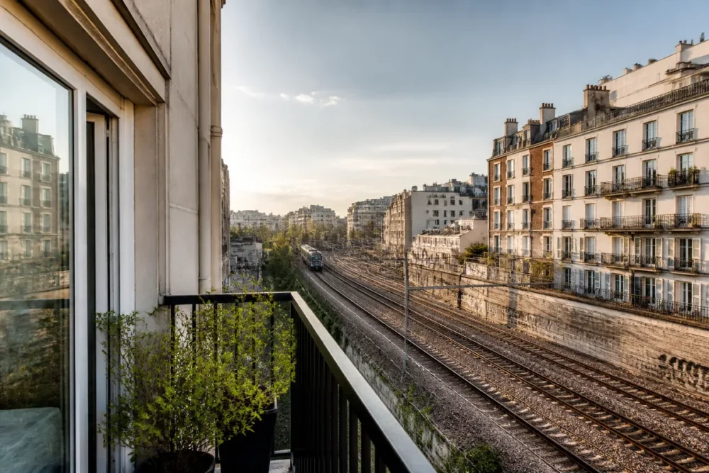 Vue réaliste depuis le balcon d’une maison montrant une voie ferrée et un train au loin