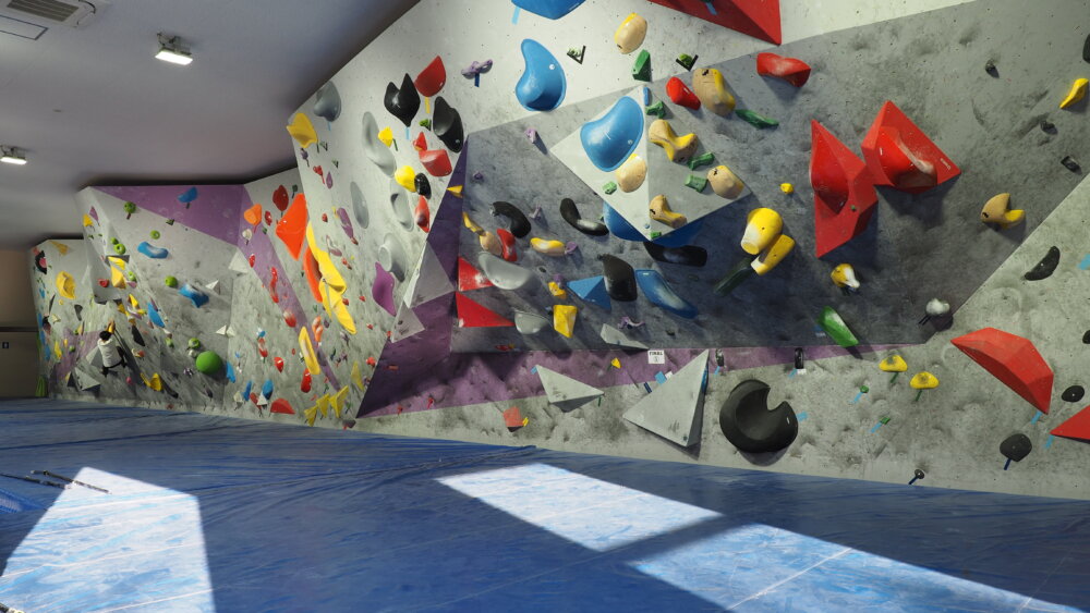 Salle de bloc avec murs inclinés, volumes colorés et grands tapis de réception